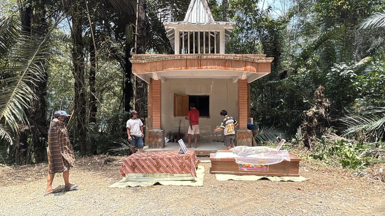 Two coffins laid out on woven mats in front of the white Patane tomb, family photographs propped against them.