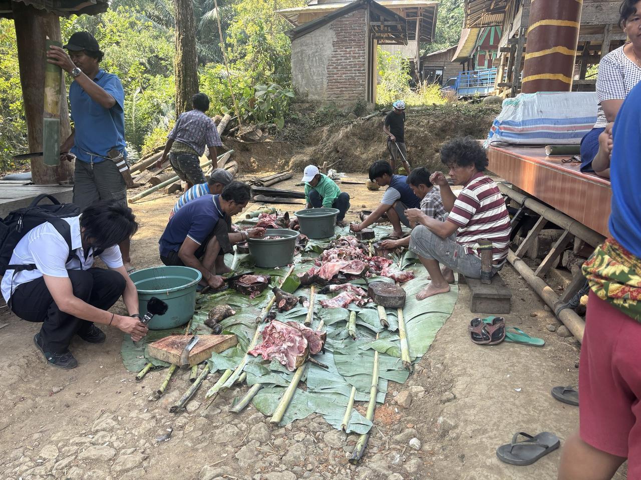 A group of men crouched around banana leaves spread with cuts of pork, working with buckets of water nearby.