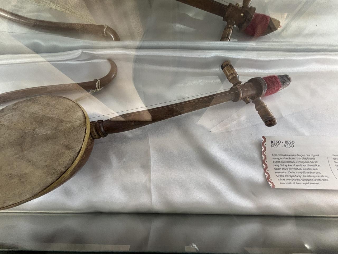 Sebuah alat musik gesek keso-keso tradisional dipajang dalam lemari kaca berdampingan dengan alat musik Sulawesi lainnya.