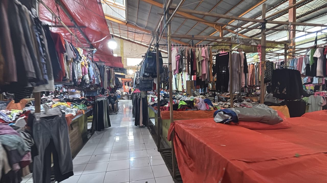 Deretan pakaian bekas tergantung di bawah lorong beratap, perdagangan pasar yang lebih biasa, hanya beberapa langkah dari meja-meja di belakangnya.