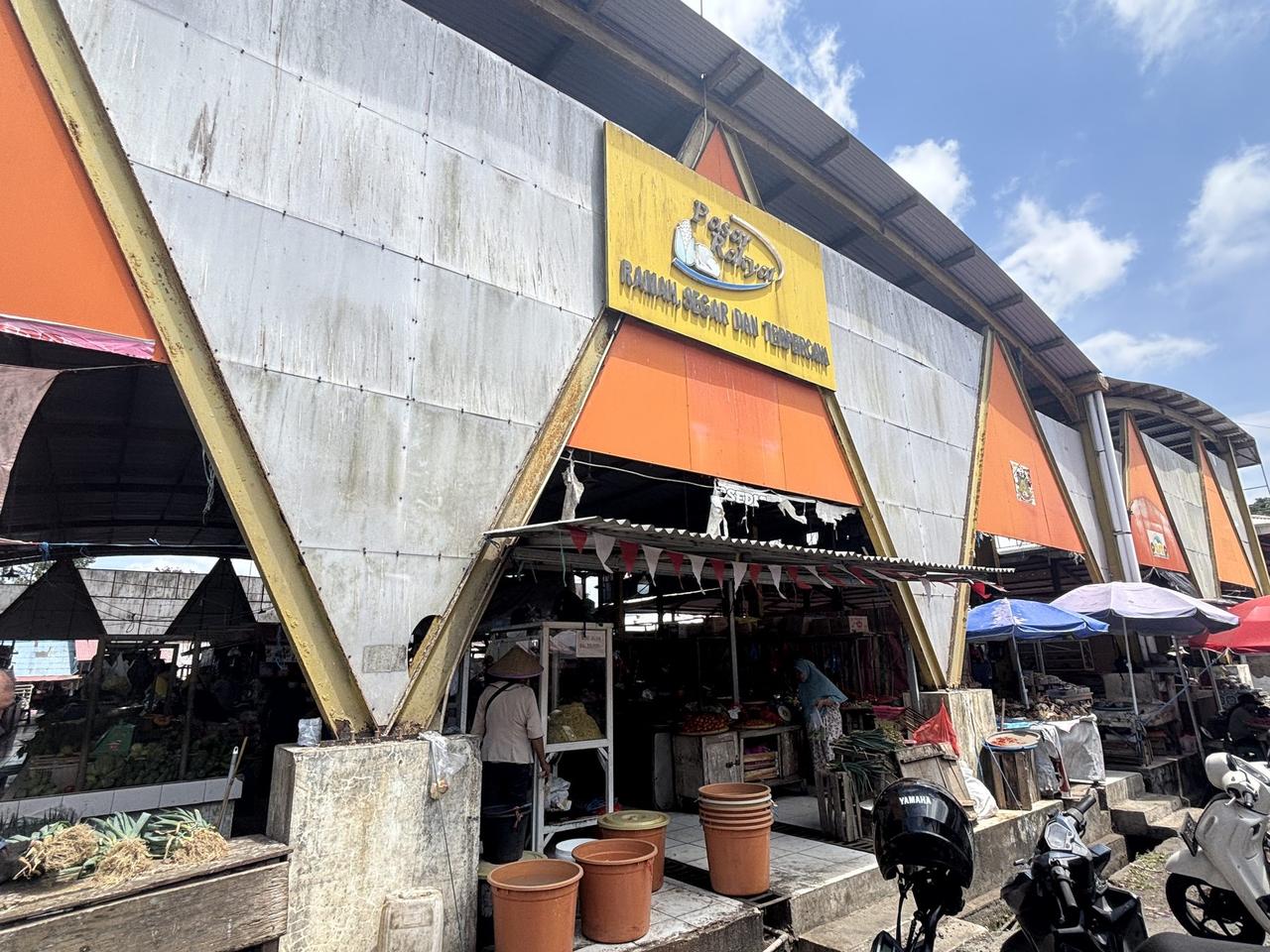 Sayap lain dari kompleks pasar, pintu masuk beratap pelana berwarna oranye-putih bertuliskan Pasar Rakyat, para pedagang sudah menata dagangan di dalamnya.