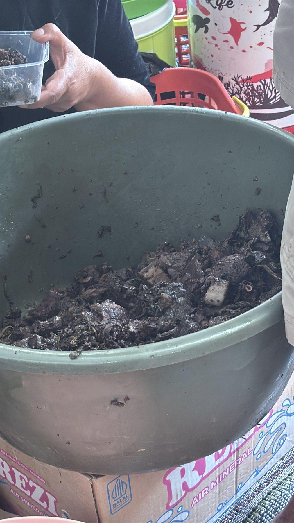 A bucket filled with cooked pieces of water buffalo meat, a hand reaching in to take a portion.
