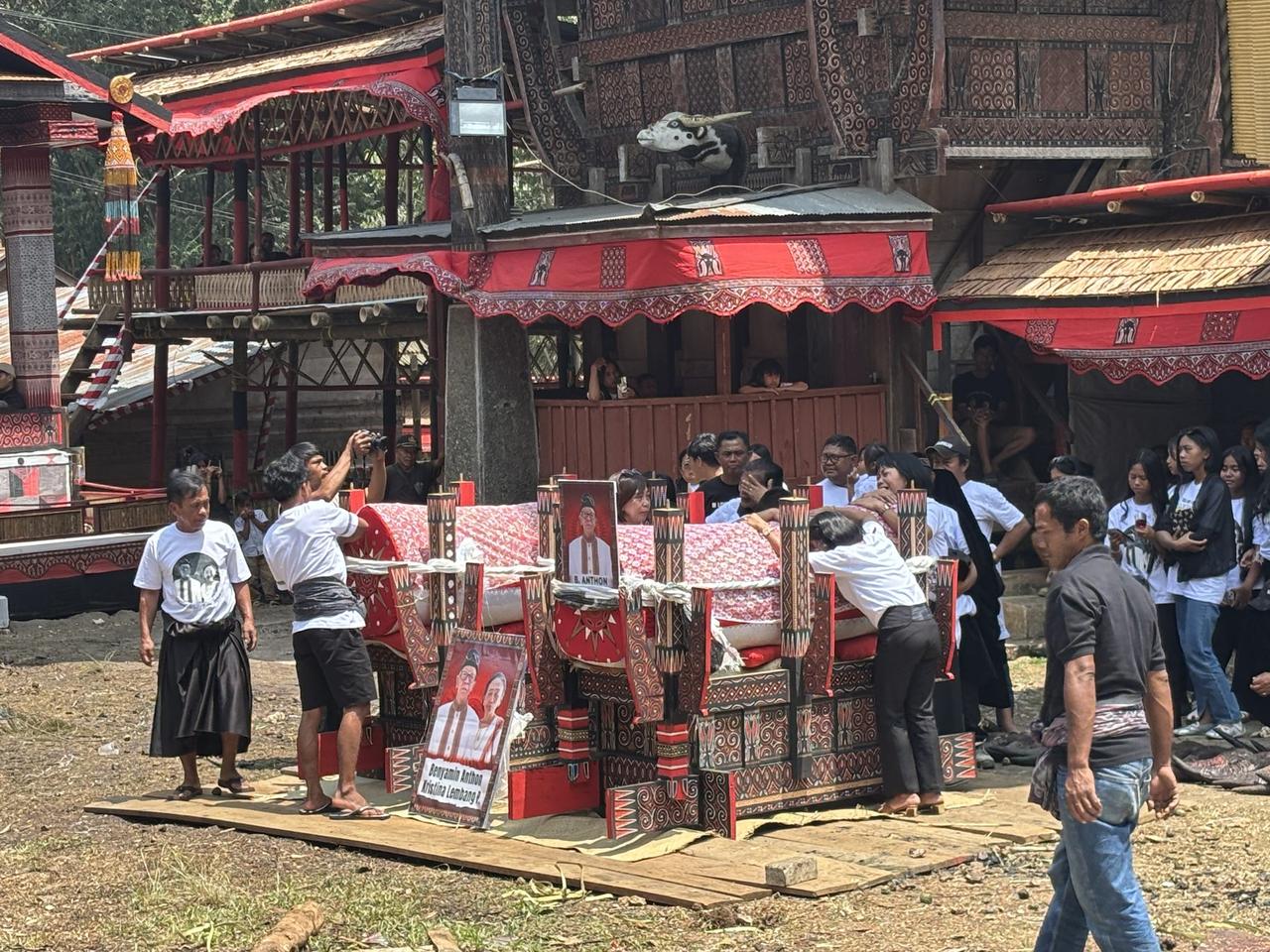 The tongkonan-shaped bier carried by many hands, a printed photograph and name card reading "B. Anthon" visible on its side.