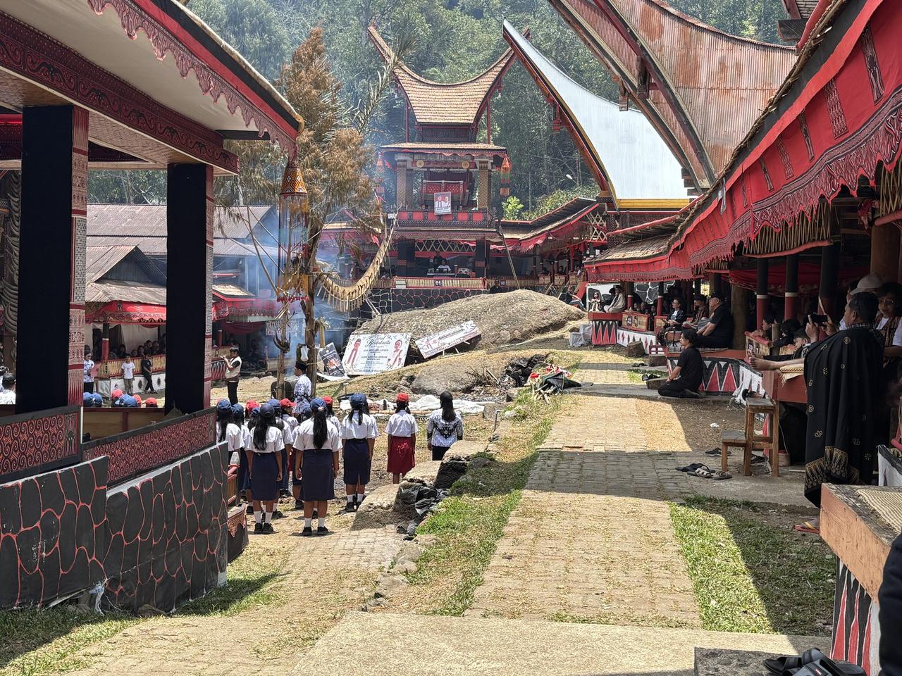 A wide view of the compound crowded with people, schoolchildren in uniform walking down a stone path toward the plaza.