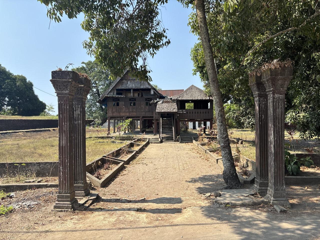 Tiang batu berukir yang telah lapuk menandai jalan masuk ke salah satu rumah adat di situs ini.