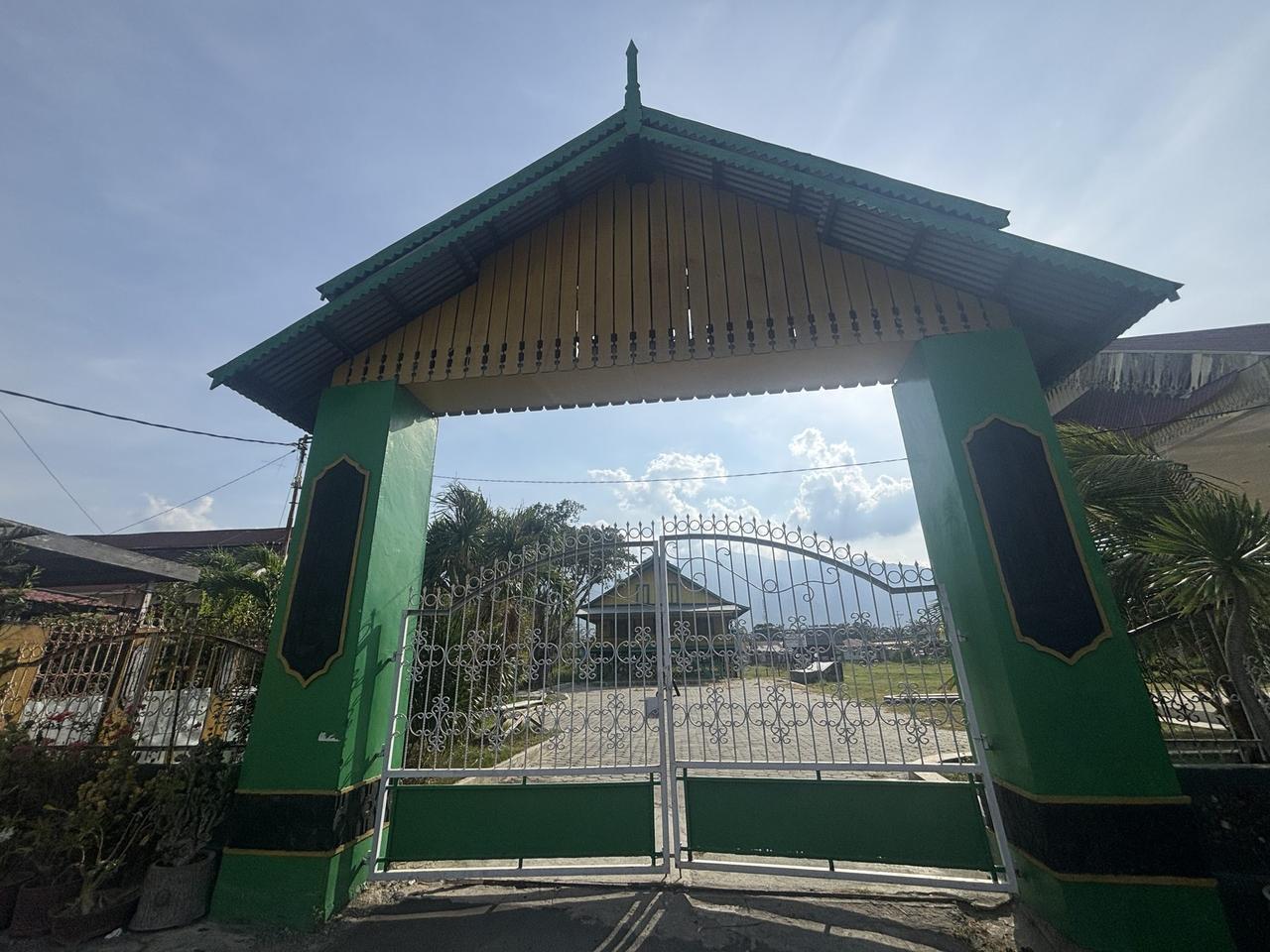 Gerbang bertingkat berwarna hijau yang menandai pintu masuk Sou Raja, dengan rumah kerajaan terlihat di seberang halaman di baliknya.