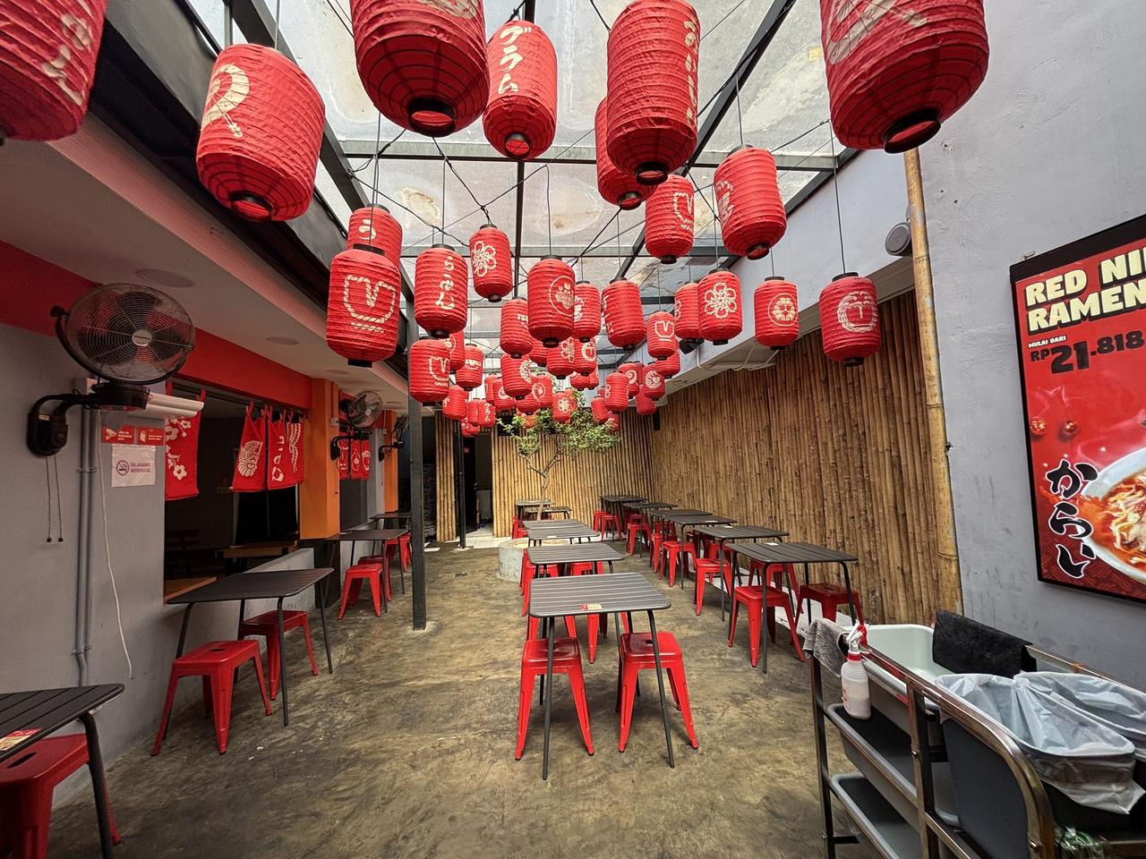 Rows of red paper lanterns hanging from a glass-roofed courtyard at a Tsuka Ramen location.