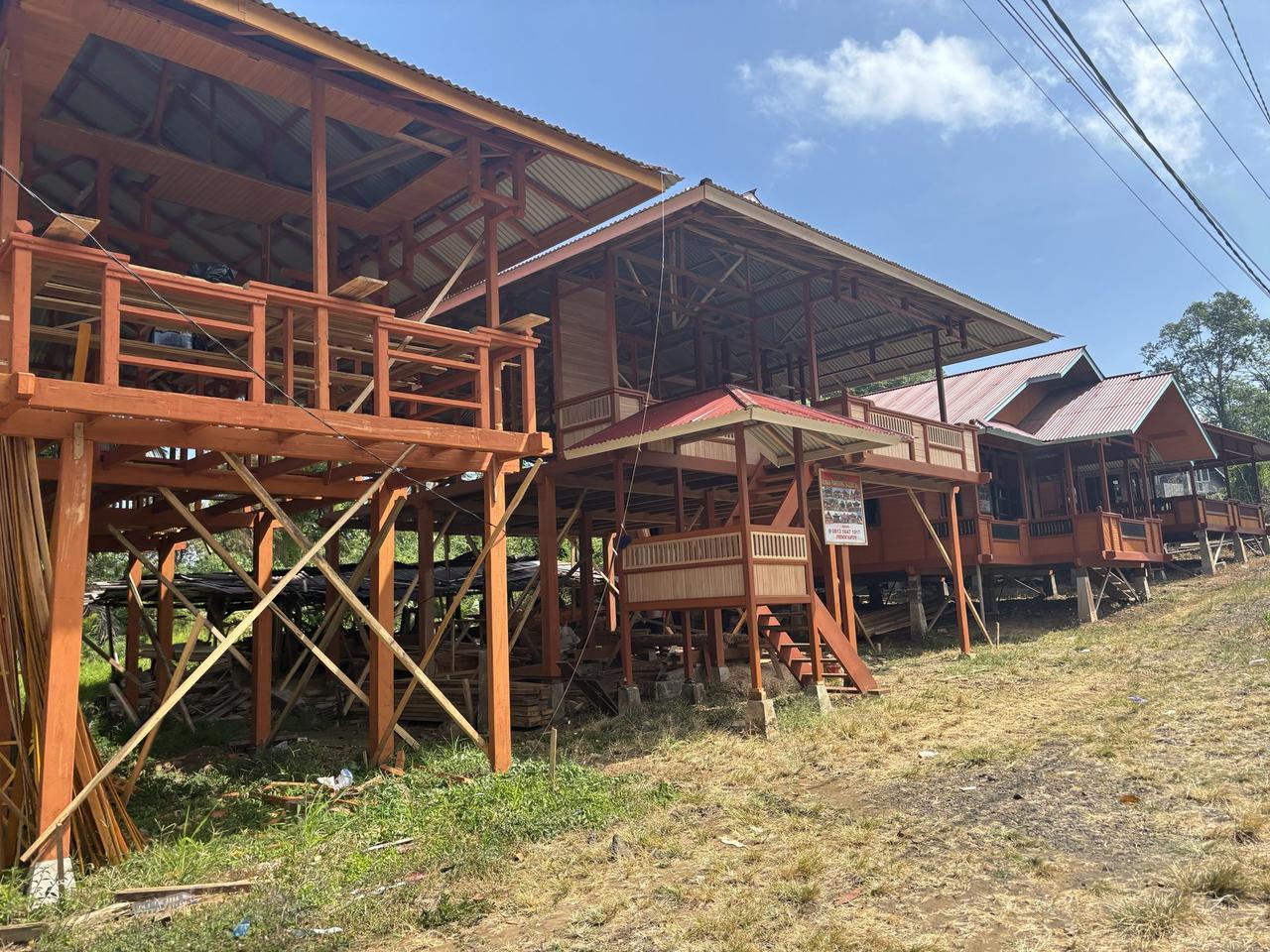 Deretan rumah kayu tradisional yang sudah jadi dan yang masih setengah dibangun berjajar di sepanjang jalan berbukit di Woloan, atap-atapnya yang bertingkat menangkap cahaya sore.