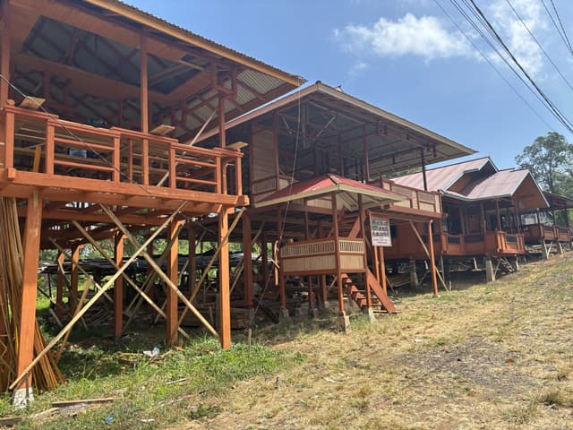 A traditional wooden house on stilts, still under construction, on a hillside.