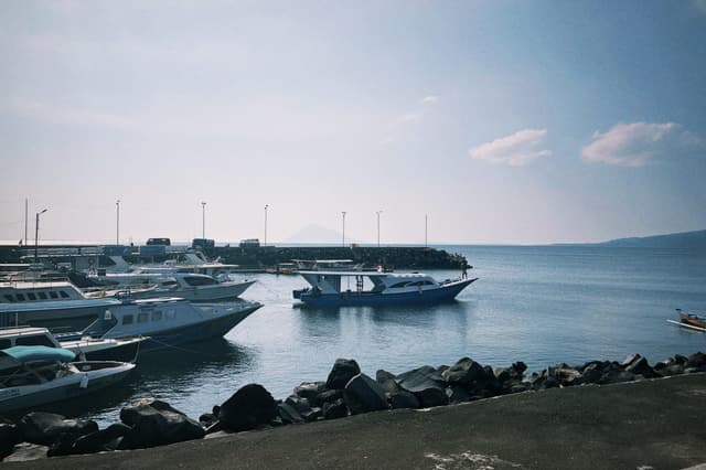 Fishing and dive boats moored in a harbor, a volcanic island rising on the horizon.