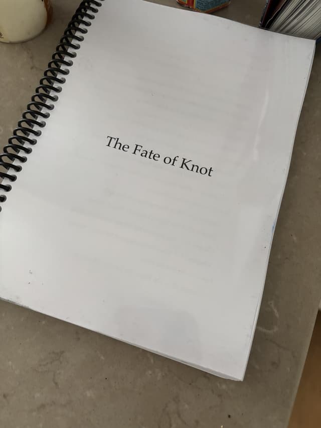 A bound manuscript titled 'The Fate of Knot' resting on a spiral binding, its title page visible on top.