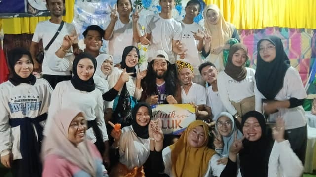 A large group photo at an Etnik Teluk cultural gathering in Indonesia, everyone smiling and posing together.