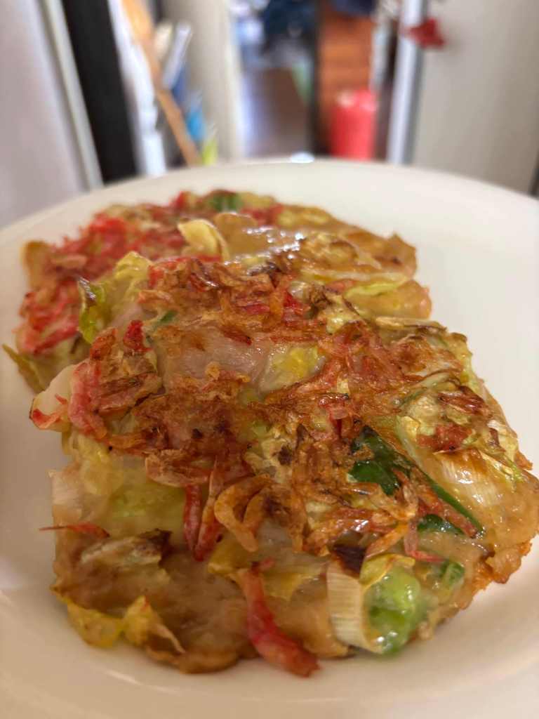 Two golden-brown fried patties with finely chopped vegetables, topped with crispy onions and served on a white plate.